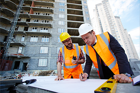 Engineers at a construction site reviewing plans, with a crane and building under construction in the background